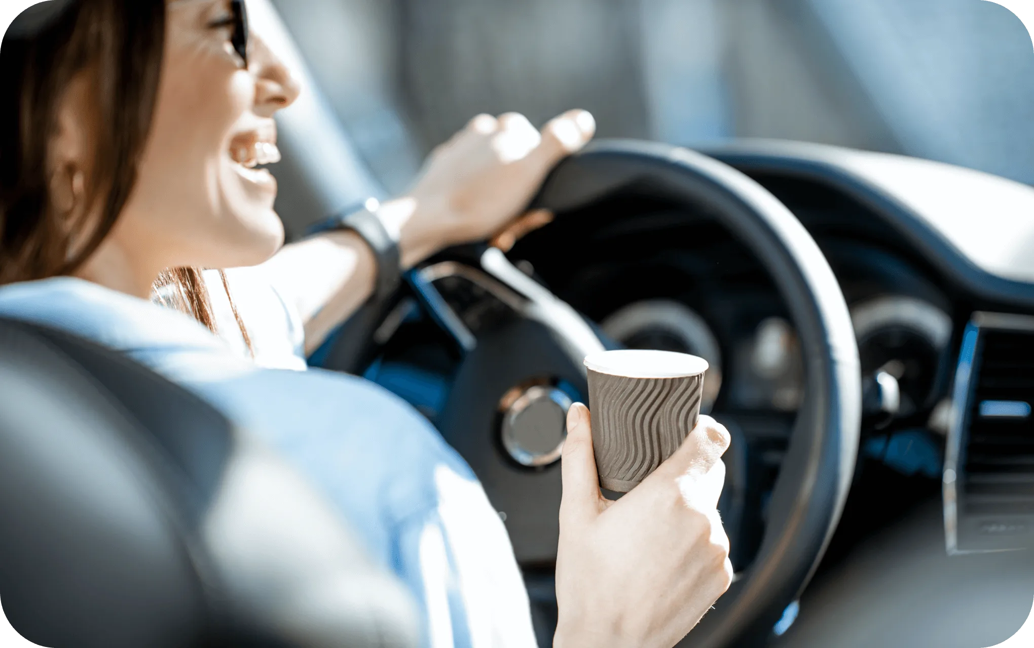 Mujer sonriendo mientras conduce un vehículo y sostiene un vaso de café.